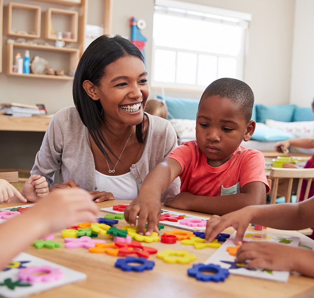A teacher is smiling while working with a young boy on a colorful activity fostering a fun and learning environment.